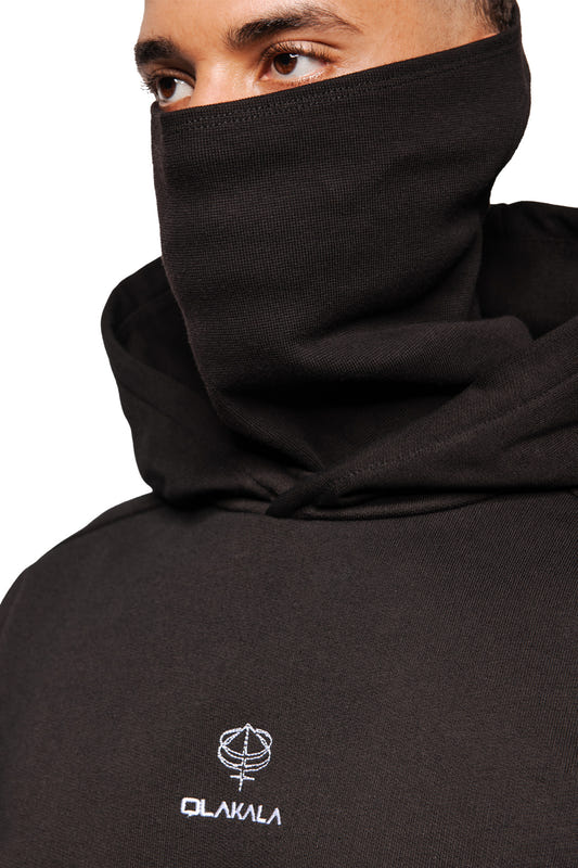 Person trägt Discreet Mask Hoodie Black mit hochgezogenem Kragen. Sichtbar sind Augen, gesticktes OLAKALA-Logo und „Defect Identity“-Icon. Oversized, cropped Passform.