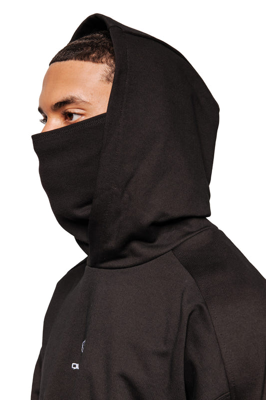 Person trägt ein Discreet Mask Hoodie Black mit integriertem Gesichtsschutz, gesticktem Defect Identity Icon, oversized und cropped Unisex-Passform.