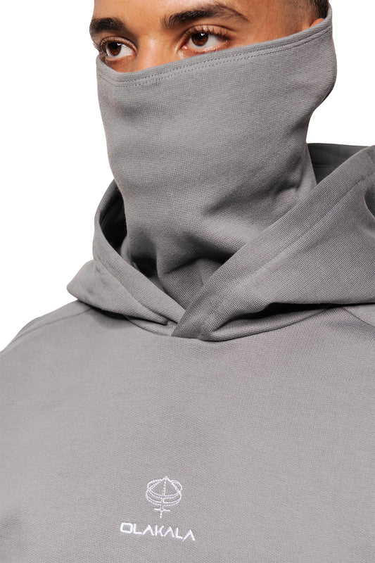 Person trägt einen Discreet Mask Hoodie Dark Gray mit hochgezogenem Kragen als Maske. Sichtbar: OLAKALA-Logo und Augenpartie. Oversized, cropped Unisex-Design.