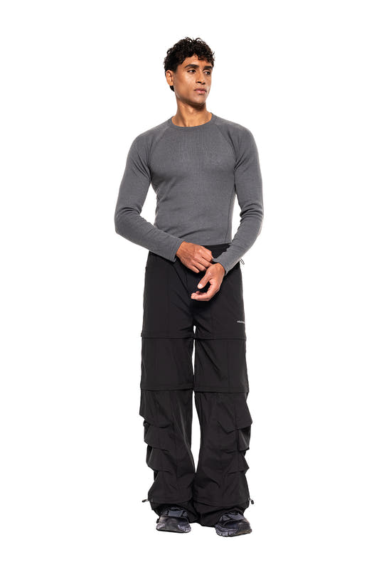 Model wears the Terra Base Layer Longsleeve Grey with a sporty cut, combined with loose black cargo pants and sneakers, ideal for versatile, sweat-wicking layering systems.