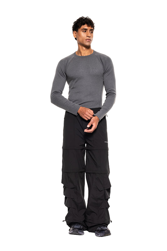 Modell trägt das Terra Base Layer Longsleeve Grau mit sportlichem Schnitt, kombiniert mit lockeren schwarzen Cargo-Hosen und Sneakern, ideal für vielseitige, schweißableitende Schichtsysteme.