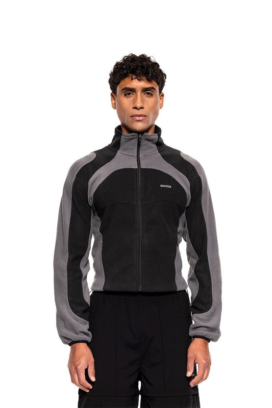 Modell trägt die Light Fleece Jacket Black & Gray mit hohem Kragen, ergonomischen Nähten und seitlichen Zip-Taschen, ideal als Midlayer für kalte Tage.