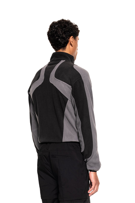 Model from behind in the Light Fleece Jacket Black & Gray with ergonomic seams and two zip pockets, combined with black pants, against a white background.