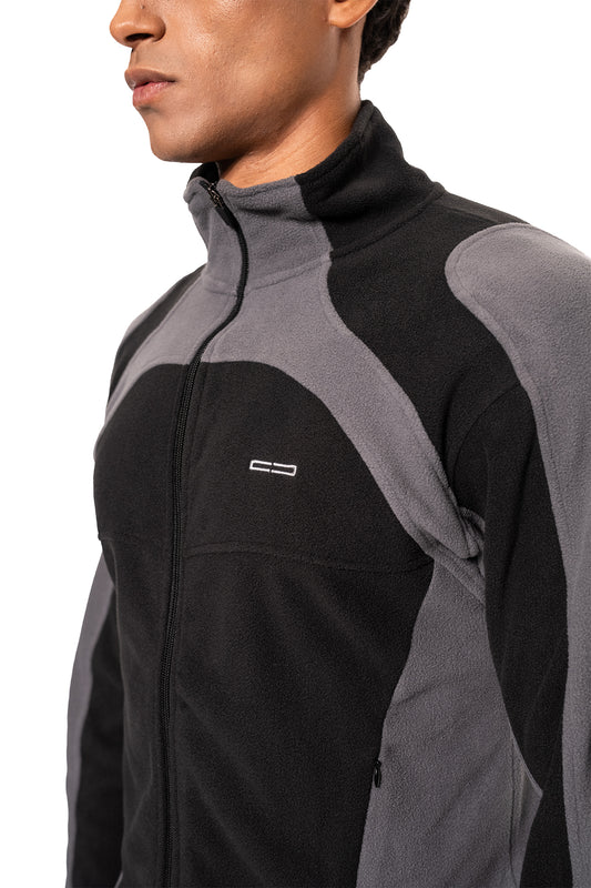 Person wears two-tone Light Fleece Jacket Black & Gray with zipper, high collar, ergonomic seams and side zip pockets, ideal as a midlayer for cold days.