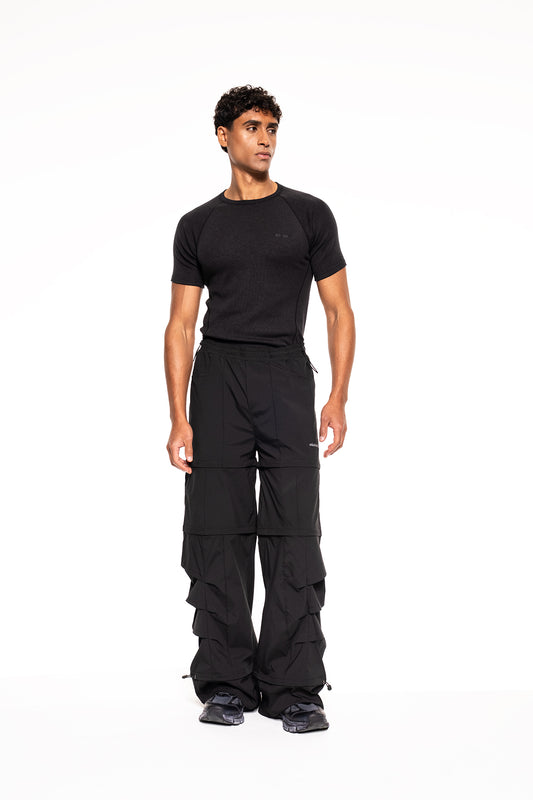 Junger Mann trägt das Terra Base Layer T-Shirt Black von OLAKALA, kombiniert mit cargo-artigen Hosen und Sneakers, ideal für funktionale Performance und vielseitigen Einsatz.