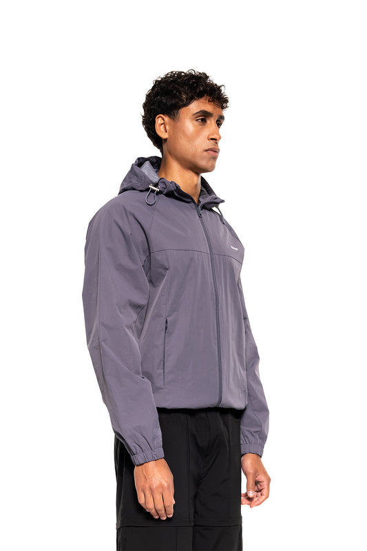 Ein junger Mann trägt den Windbreaker Icon Gray mit Kapuze, verstellbaren Kordelzügen und Reißverschlusstaschen, ideal für Sport und Alltag.