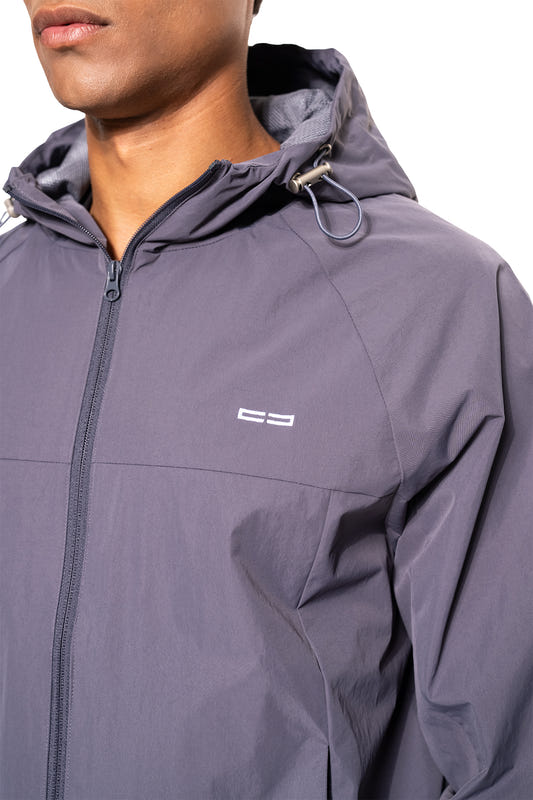 Person trägt den Windbreaker Icon Gray mit Kapuze, Kordelzügen und Reißverschluss, ideal für Sport und Alltag, mit kleinem Logo auf der Brust.