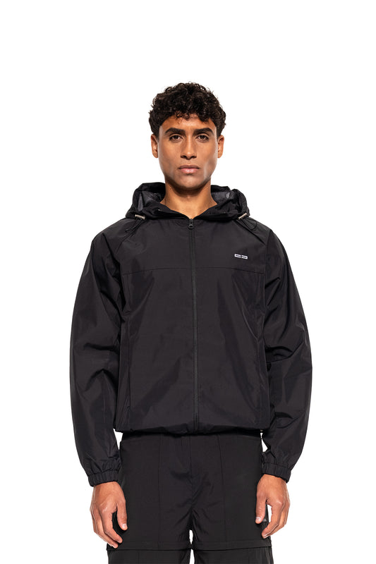 Männliches Modell trägt Windbreaker Icon Black mit Kapuze, elastischen Bündchen und Saum, ideal für Sport und Alltag, präsentiert von OLAKALA.