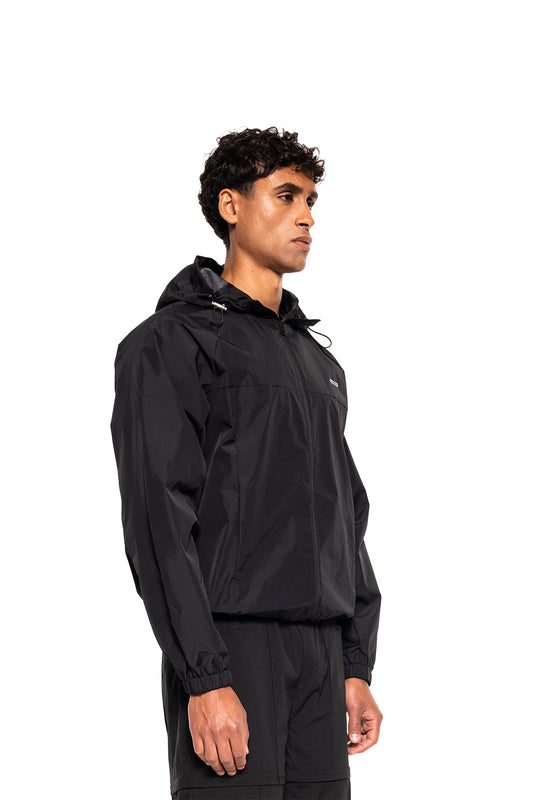 Mann trägt Windbreaker Icon Black, sportlich geschnittene, wasserabweisende Jacke mit Kapuze und Kordelzügen, ideal für Outdoor-Aktivitäten und urbanen Stil.