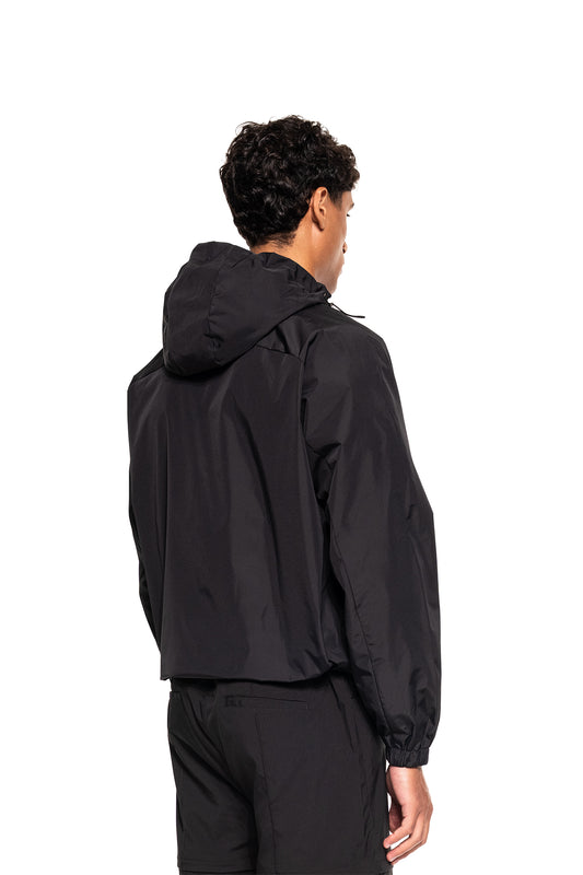 Ein junger Mann trägt den Windbreaker Icon Black, einen sportlichen, funktionalen Kapuzen-Windbreaker mit elastischen Bündchen und verstellbaren Kordelzügen, ideal für Outdoor-Aktivitäten.