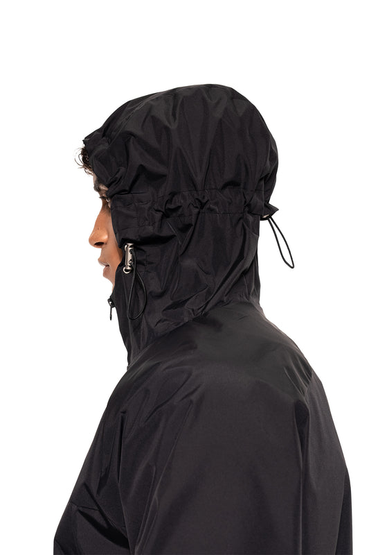 Person trägt den Windbreaker Icon Black mit Kapuze und Kordelzug, ideal für Sport und Alltag. Wasserabweisend und leicht, bietet Bewegungsfreiheit und modernen Stil.