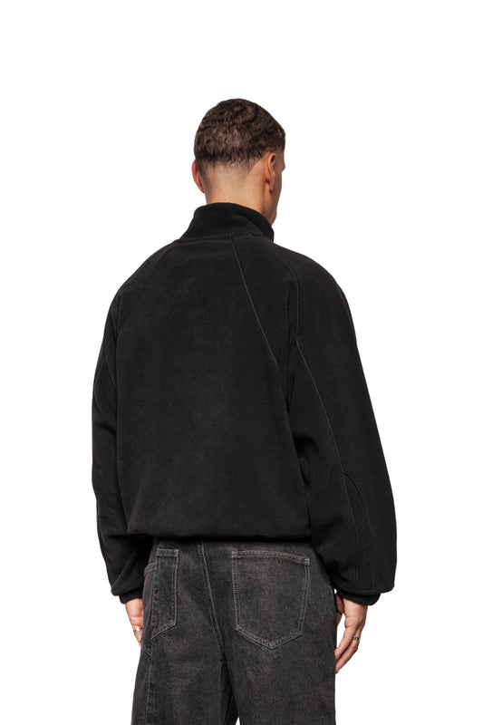Person from behind in Fleece Jacket Black Onyx with raglan sleeves and elastic cuffs, combined with straight-cut jeans. Hands loose at the sides.
