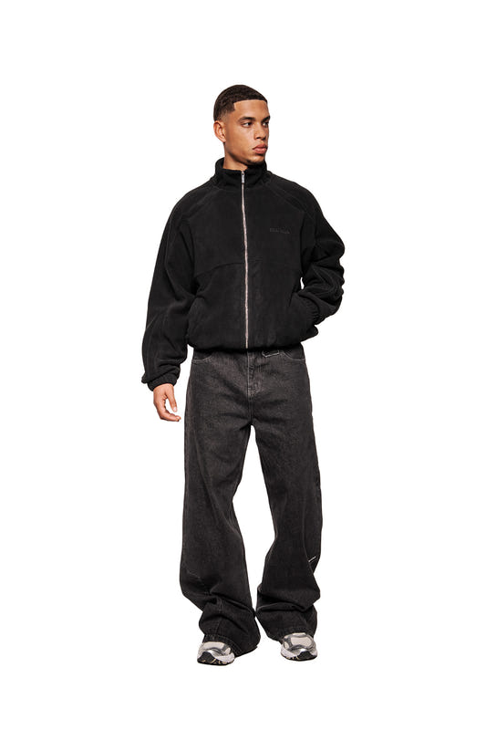 Male model wearing Fleece Jacket Black Onyx with high collar, embroidered logo, slit pockets and elasticated cuffs. Combine with wide denim and sneakers.