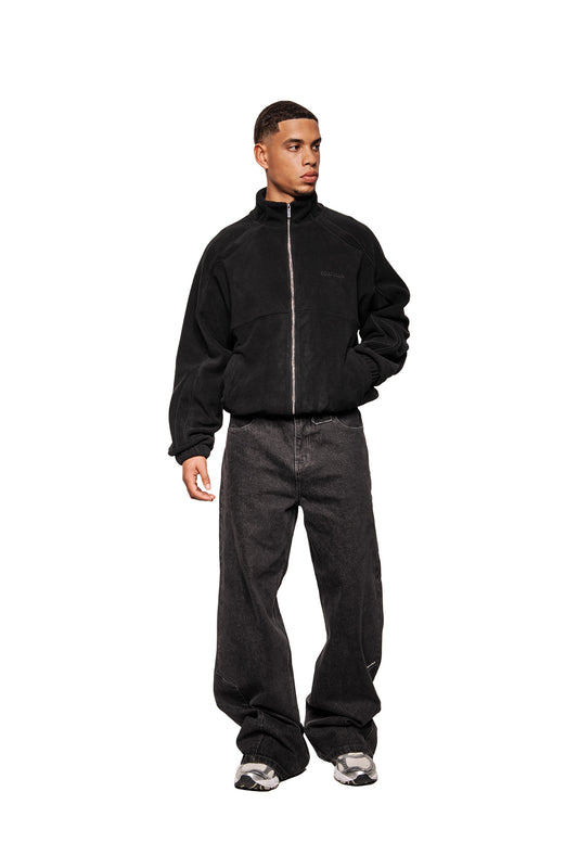 Male model wearing Fleece Jacket Black Onyx with high collar, embroidered logo, slit pockets and elasticated cuffs. Combine with wide denim and sneakers.