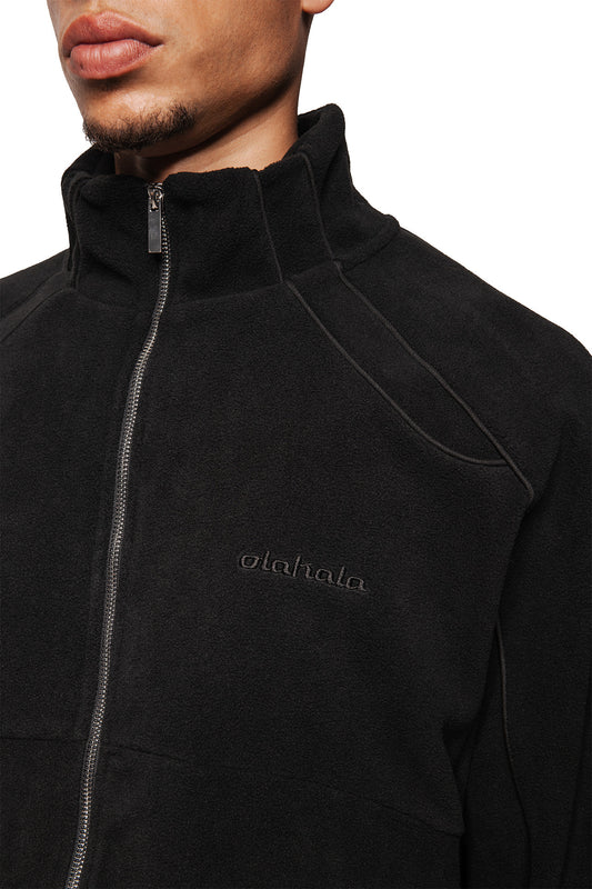 Person wears Fleece Jacket Black Onyx with stand-up collar, silver zipper, embroidered olalala logo on the chest, raglan seams and elastic cuffs.
