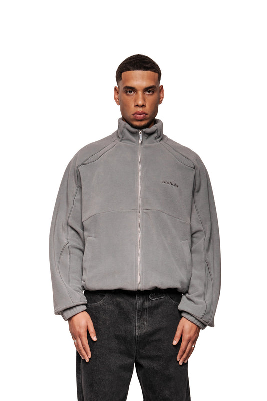 Modell trägt die Fleece Jacket Night Owl mit hohem Kragen, OLA KALA-Stickerei, vorderen Eingriffstaschen und elastischen Bündchen. Oversized Fit, unisex.
