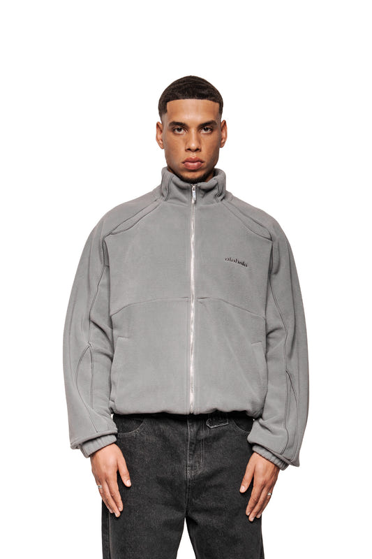 A young man wears the Night Owl fleece jacket with high collar, elasticated cuffs and OLA KALA logo, combined with dark jeans.