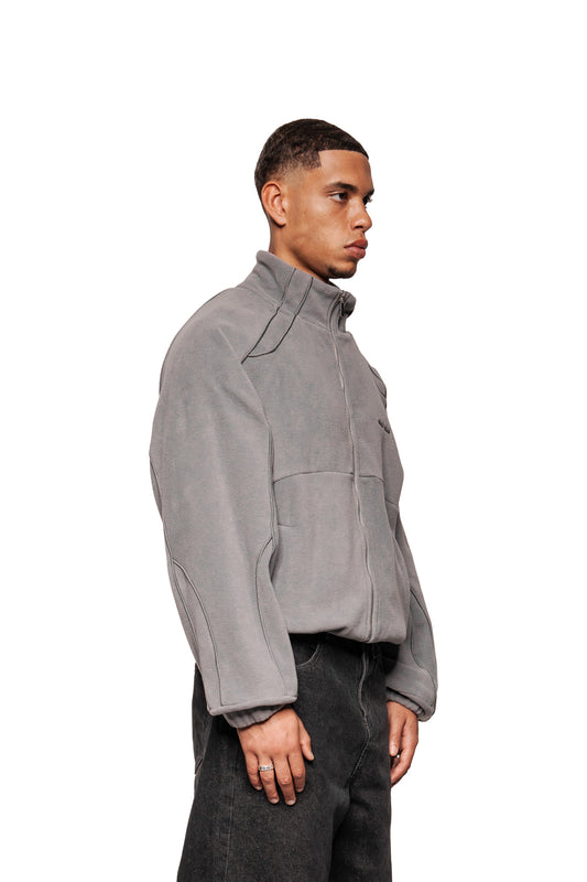 Männermodell im Profil trägt Fleece Jacket Night Owl mit hohem Kragen, OLA KALA-Logo, Taschen und elastischen Bündchen, kombiniert mit dunklen Jeans.