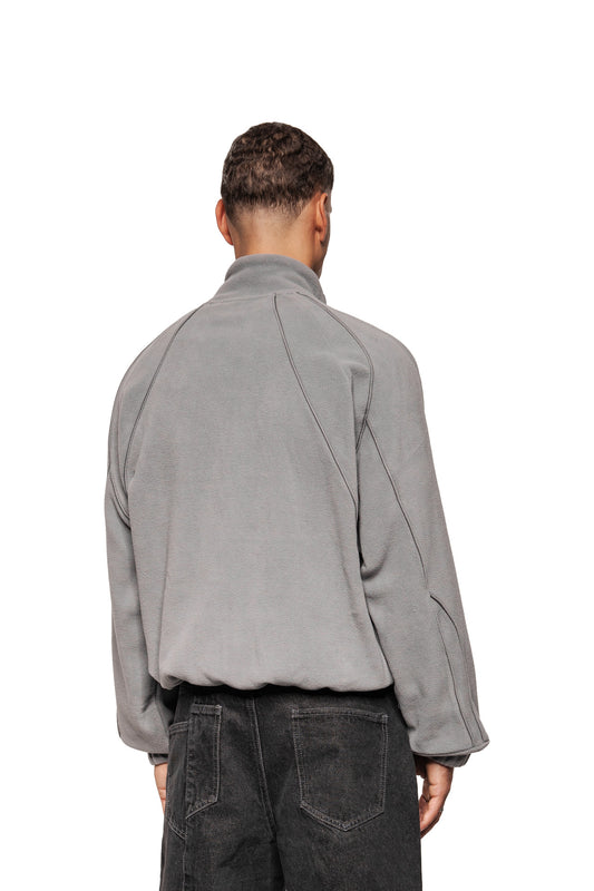 Person trägt Fleece Jacket Night Owl mit hohem Kragen, Raglanärmeln, Teilungsnähten und OLA KALA-Logo-Stickerei, kombiniert mit dunklen Jeans.
