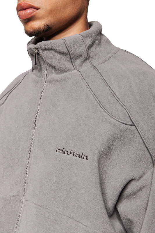 Person trägt Fleece Jacket Night Owl mit OLA KALA-Logo auf der Brust, Eingriffstaschen, elastischen Bündchen und oversized Unisex-Passform.