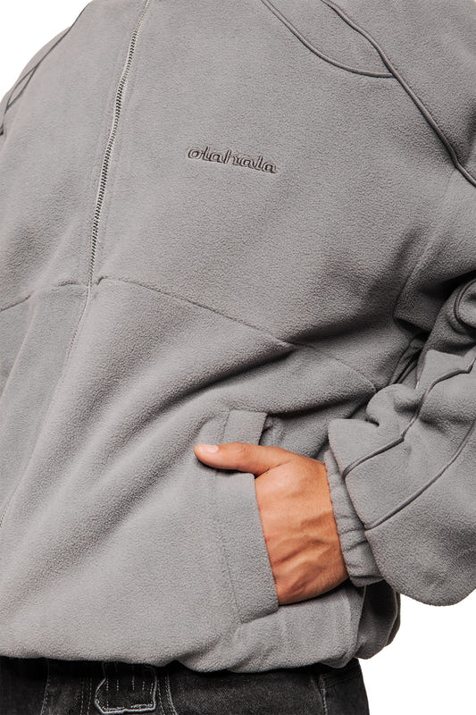 Person wears the Night Owl fleece jacket with OLA KALA embroidery, zipper, kangaroo pocket, elastic cuffs and oversized fit. Hand rests in the pocket.