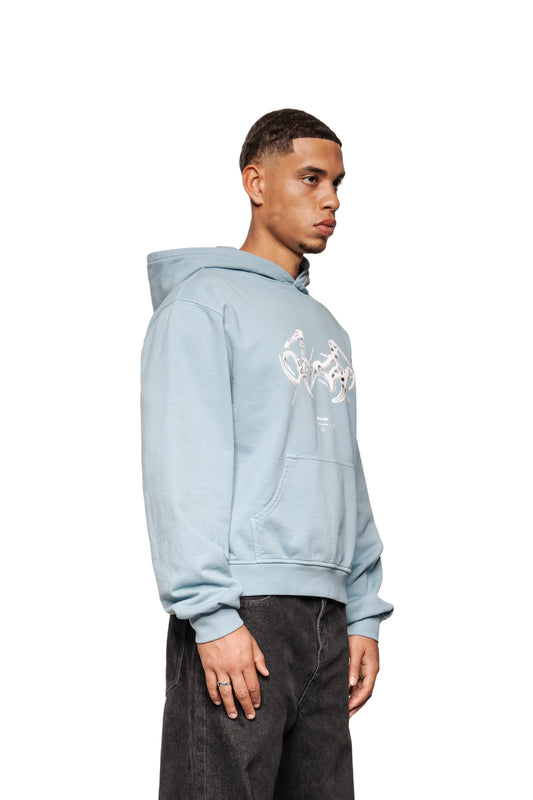 Junger Mann in Profilansicht trägt den Fusion Hoodie Blue mit Kängurutasche und „Fusion“-Grafik, kombiniert mit locker sitzenden Jeans.