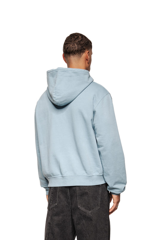 Person von hinten im Fusion Hoodie Blue mit Ripp-Bündchen, Kängurutasche und flacher Kapuze, kombiniert mit locker sitzenden, schwarz gewaschenen Jeans.