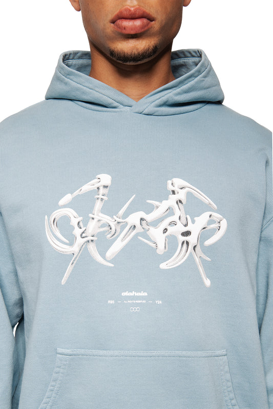 Person trägt das Fusion Hoodie Blue mit spitzem Grafikdruck und „aloha“ Schriftzug. Sichtbare Kängurutasche, Ripp-Bündchen an Ärmeln und Saum. Unisex, reguläre Passform.