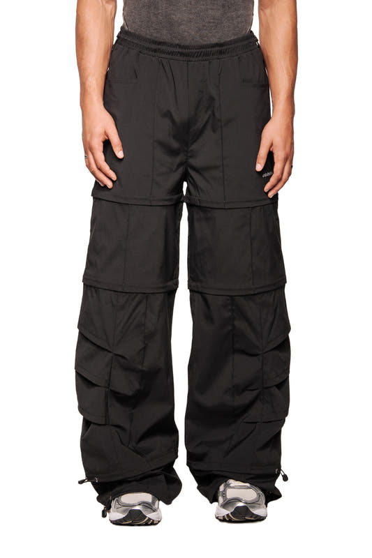 Person wears Gills Zip-Off Pants Black with detachable leg panels, elastic waistband, drawstrings at ankles, square pockets, combined with ribbed sleeveless top and sneakers.