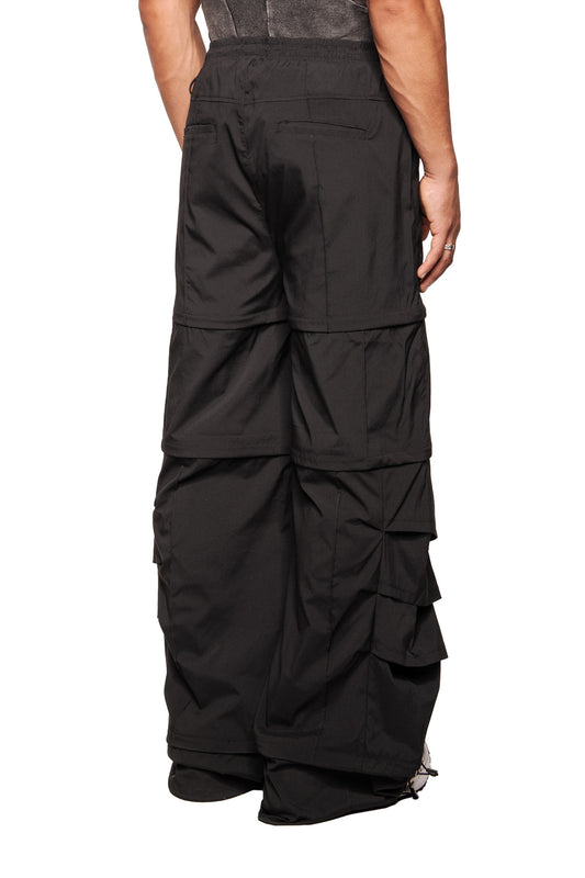 Person wears Gills Zip-Off Pants Black with detachable leg sections, large side pockets and elastic waistband, combined with a dark sleeveless top and white sneakers.