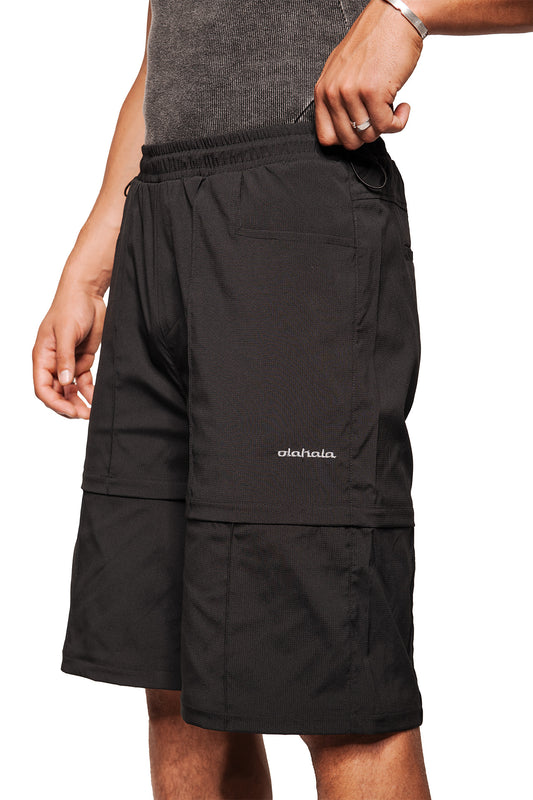Person wears Gills Zip-Off Pants Black by OLAKALA with elastic waistband and detachable leg sections made of robust rip-stop fabric, embroidered logo visible.