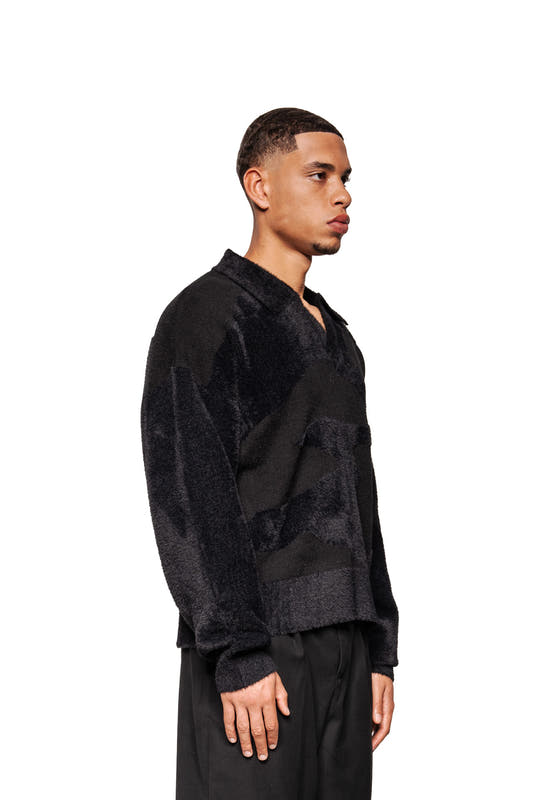 Young man in Glitched Fuzzy Polo Black with buttonless polo collar, ribbed cuffs and embroidered Synergy logo, minimalist style by OLAKALA.