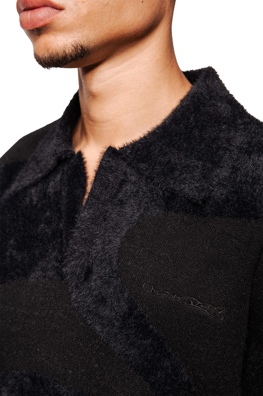 Man wears Glitched Fuzzy Polo Black with fluffy collar, embroidered Synergy logo, knitted ribbed cuffs, unisex, regular fit.