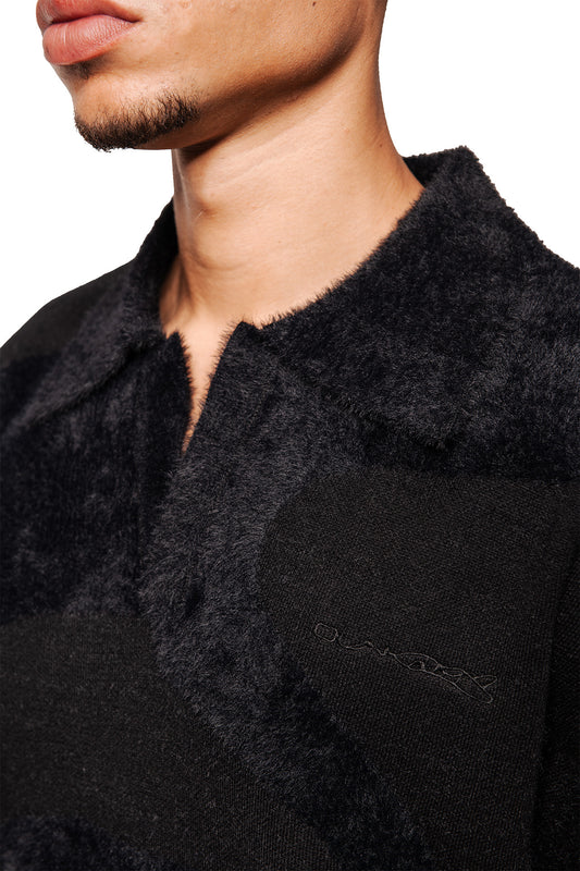 Man wears Glitched Fuzzy Polo Black with fluffy collar, embroidered Synergy logo, knitted ribbed cuffs, unisex, regular fit.