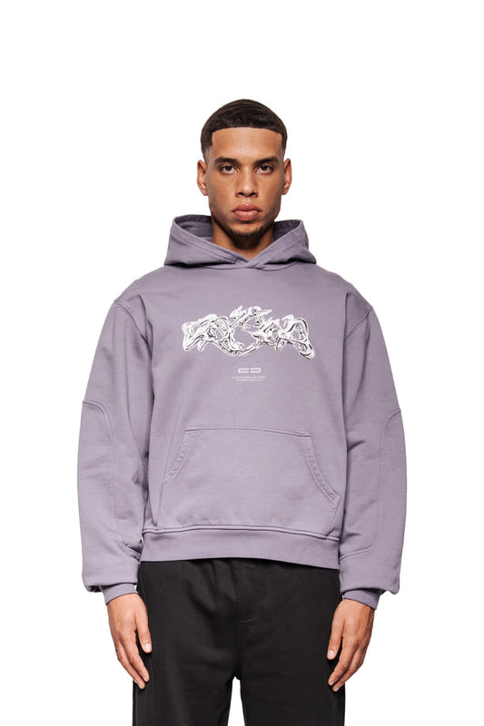 Man wears the Greyzone Hoodie Lilac with abstract graphics, kangaroo pocket and ribbed cuffs. Relaxed fit, combined with black pants.