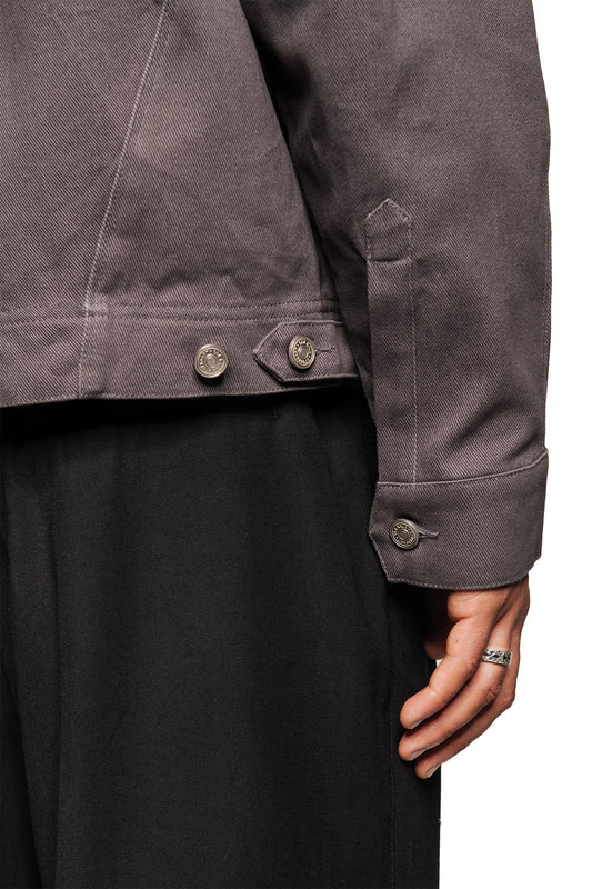 Close-up of a gray Heavy Anatomy cotton overshirt with press studs, loose cut and embroidered OLAKALA logo on the breast pocket, worn over black pants.