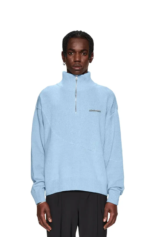 Person trägt einen CC Knit Halfzip Light Blue Pullover mit verschiedenen Strickmustern, überschnittenen Schultern, versetztem Saum und Metallpin, präsentiert im OLAKALA Stil.