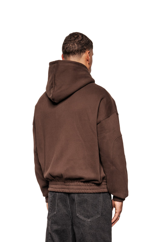Rückansicht eines Mannes im Isolation Zip Hoodie Brown mit elastischem Saum, Oversized-Passform, Reißverschluss und Teilungsnähten. Hände locker an den Seiten.