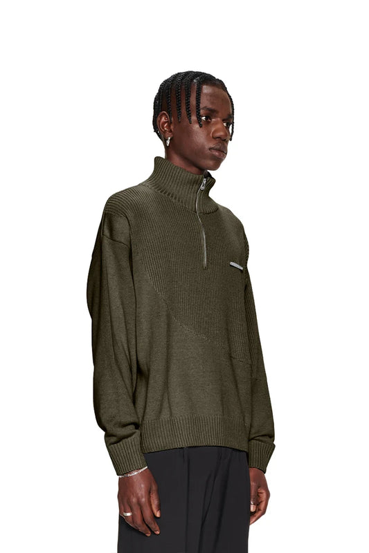 Mann in grünem CC Knit Halfzip Khaki, zeigt Strickpullover mit verschiedenen Mustern, überschnittenen Schultern und OLAKALA-Metallpin.
