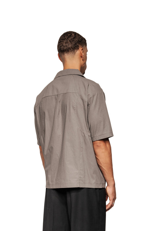 Back view of a model in the Layered Short Sleeve Shirt Gray with Cuban collar, back seam detail and loose fit, combined with black pants.