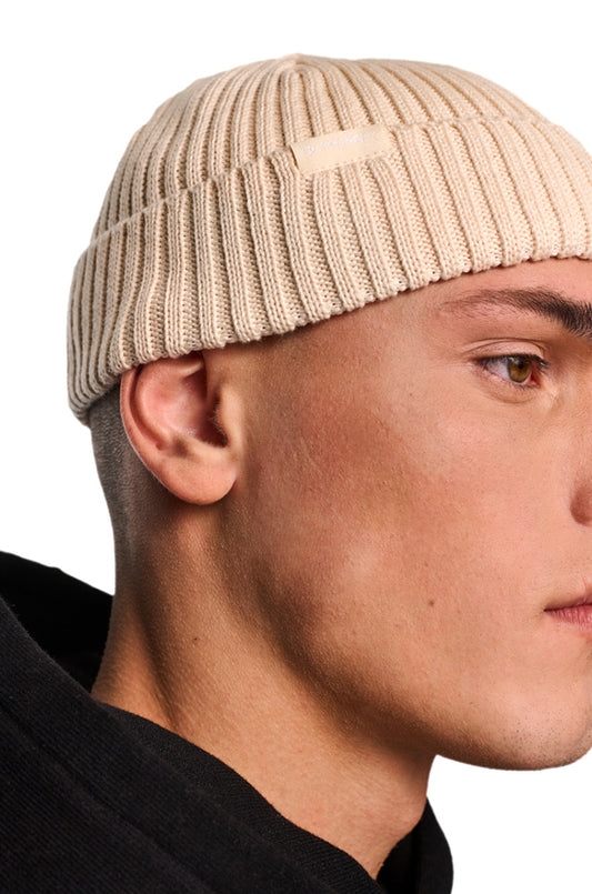 Mann trägt Alien Intel Beanie Beige im gerippten Fisherman-Stil mit gewebtem OLAKALA-Label, Nahaufnahme auf Gesicht und Beanie.