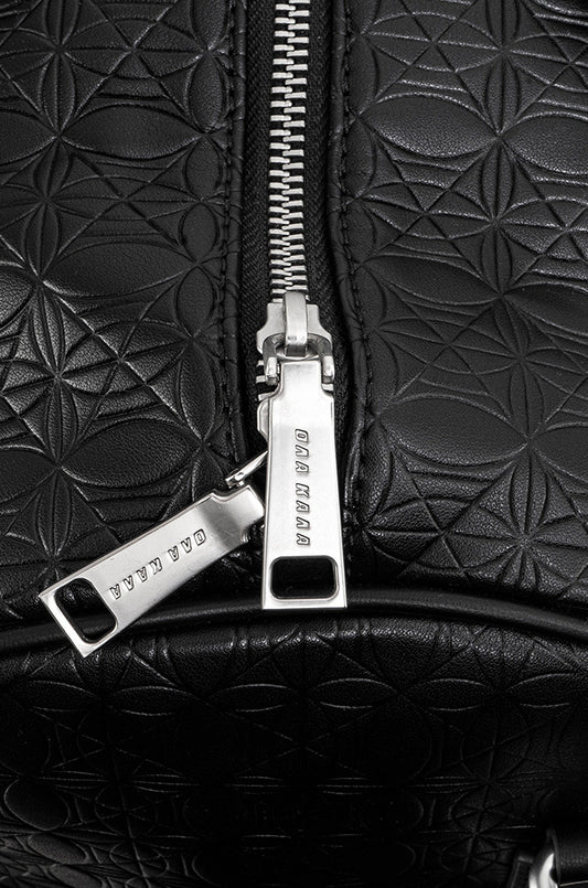 CC Debossed Weekender Bag Black mit OLAKALA-Monogramm, Metallreißverschluss und abnehmbarem Schulterriemen. Detailansicht des Reißverschlusses und Schlüsselanhängers.