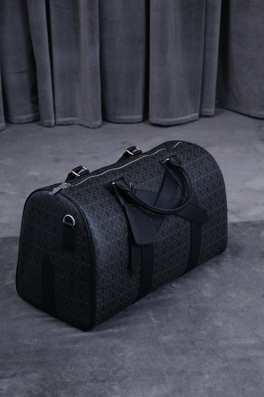 Schwarze Duffle-Bag mit geometrischem Muster, zwei Griffe und Schultergurt, liegt auf grauem Boden vor dunklen Vorhängen.