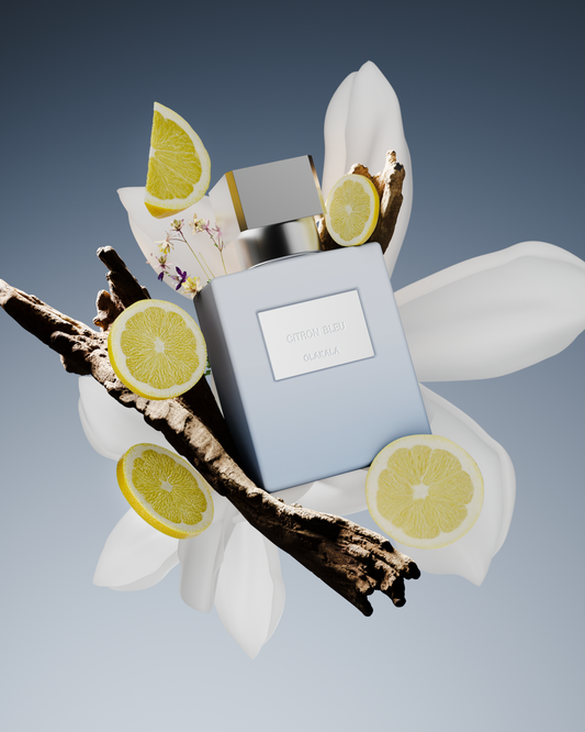 Parfumflakon Citron Bleu von OLAKALA in hellem Blau mit silberner Kappe, von Zitronenscheiben, Vanillezweigen und weißen Blüten umgeben vor blauem Hintergrund.
