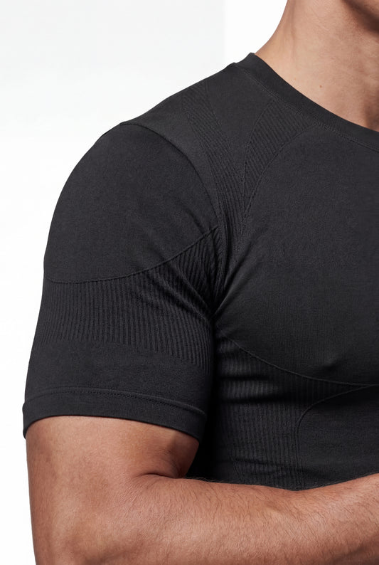 Person trägt ein schwarzes Compression T-Shirt mit gerippten Details und nahtloser Konstruktion, betont muskulöse Linien für optimale Bewegungsfreiheit und Komfort.