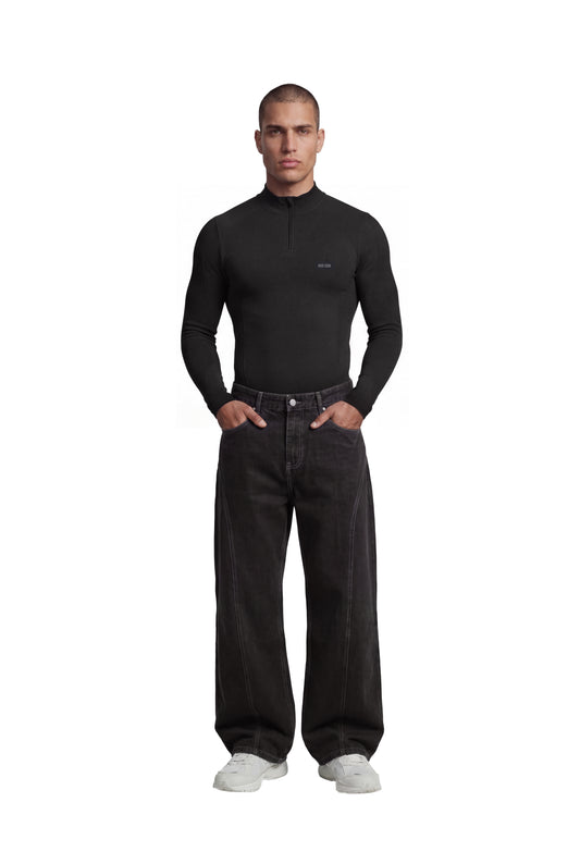 Männermodell trägt OLAKALA Compression Halfzip Black: eng anliegendes, nahtloses Design mit kurzem Reißverschluss, kombiniert mit locker sitzenden Jeans und weißen Sneakers.