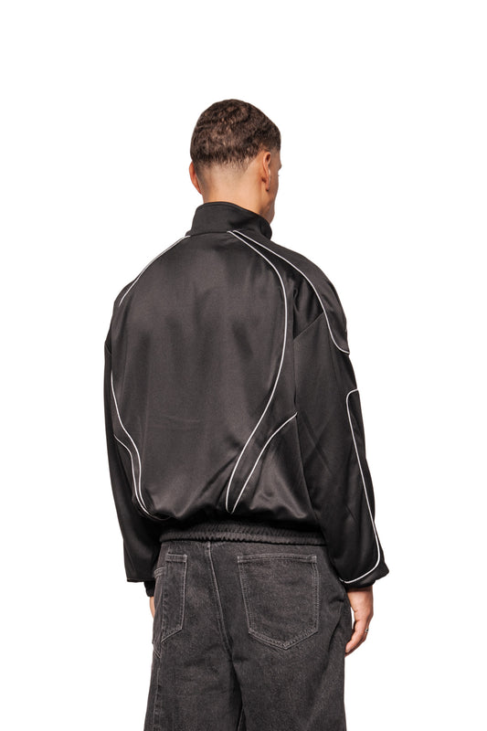 Rückansicht des Rave Trackjacket Black mit reflektierenden Paspelierungen und Stehkragen, getragen von einem Modell, kombiniert mit dunkelgrauen Jeans.
