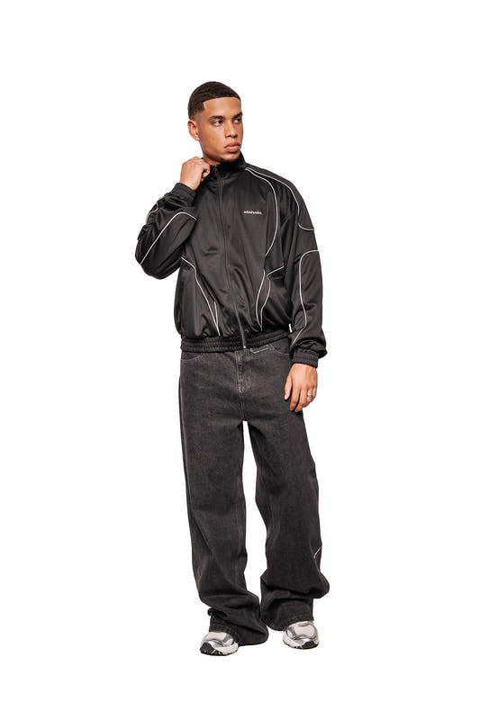 One model wears the Rave Trackjacket Black with stand-up collar, reflective dividing seams and embroidered OLAKALA logo, combined with casual jeans and sneakers.