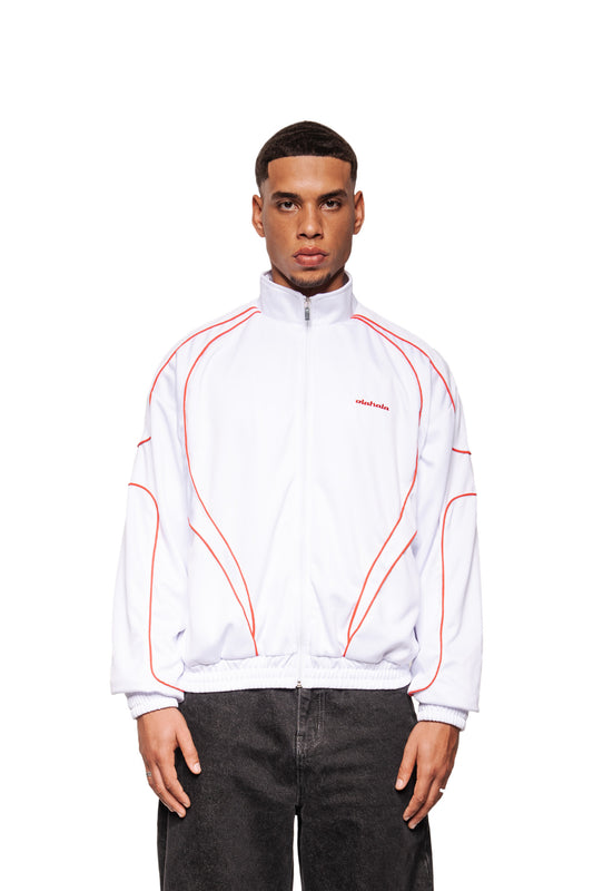 Junger Mann trägt weißes Rave Trackjacket mit roter Paspelierung und gesticktem OLAKALA Logo, kombiniert mit dunklen Hosen.