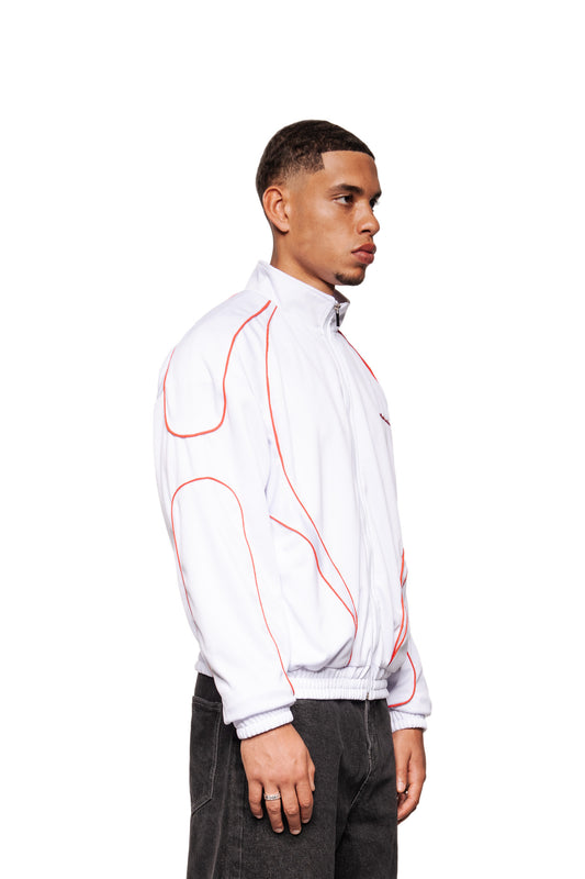 Junger Mann im Profil mit weiß-rotem Rave Trackjacket von OLAKALA, featuring Stehkragen, Reißverschluss und Paspelierungen, kombiniert mit dunklen Jeans.